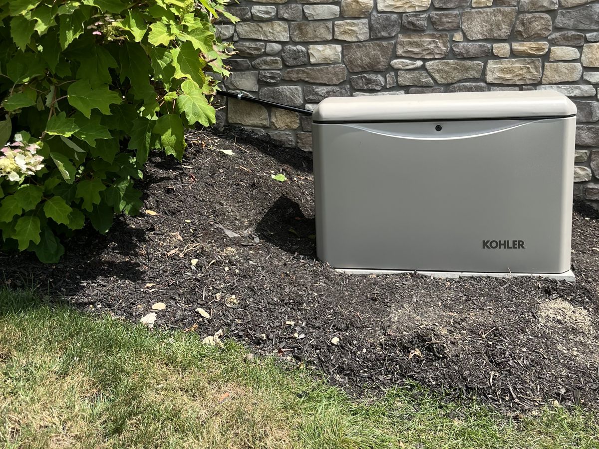 Kohler home standby generator installed on a concrete pad beside a stone-veneer home